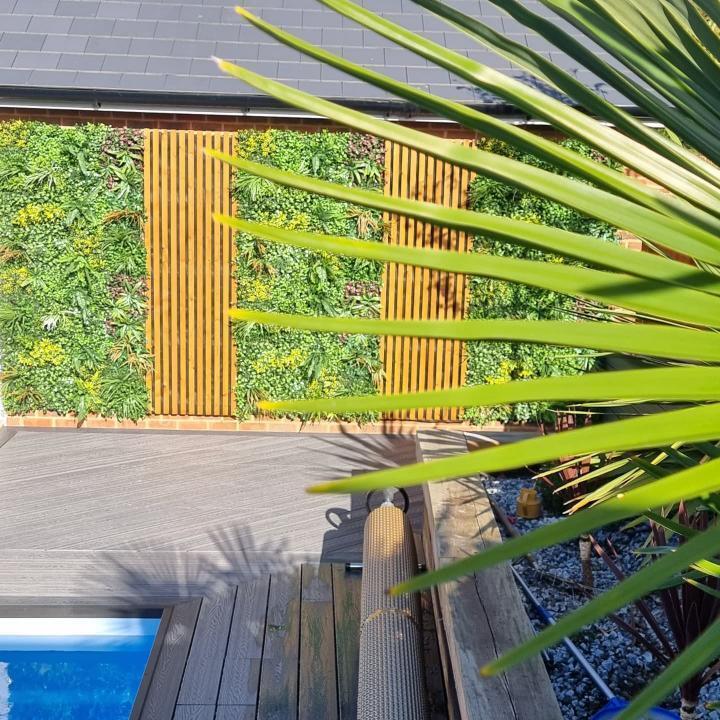 Artificial green wall panel with dense variegated leaves, seen from a backyard patio