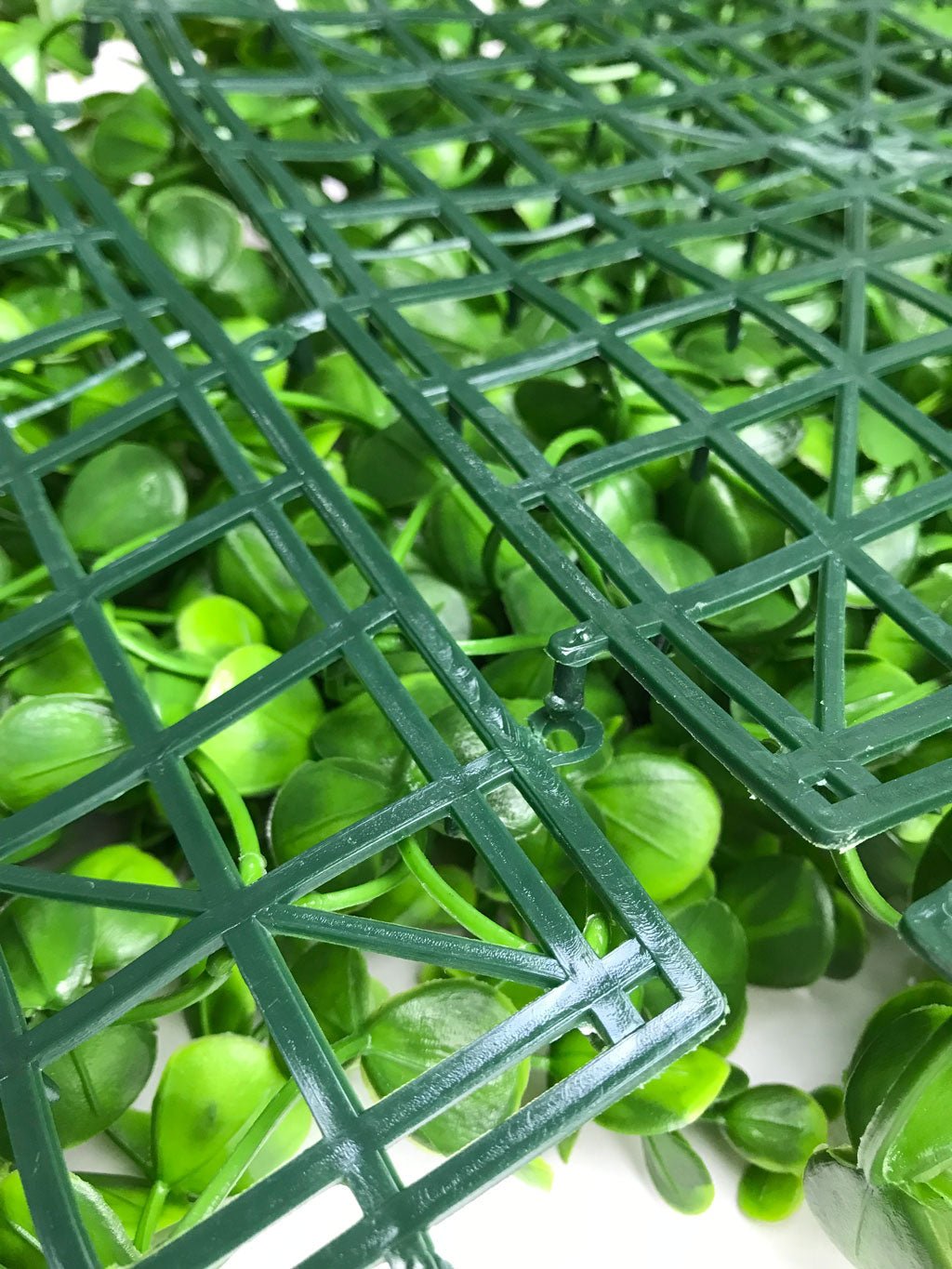 Artificial green plant wall panel with dark green grid and leaf cluster texture