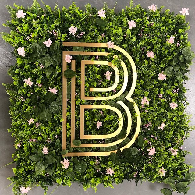 Artificial green plant wall panel with golden monogram B cutout and pink flowers