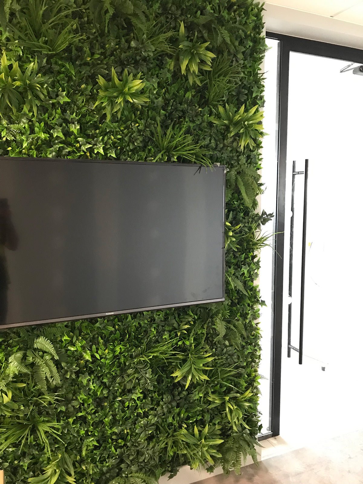 Artificial green wall panel with dense faux ivy leaves and layered grasses, variegated foliage