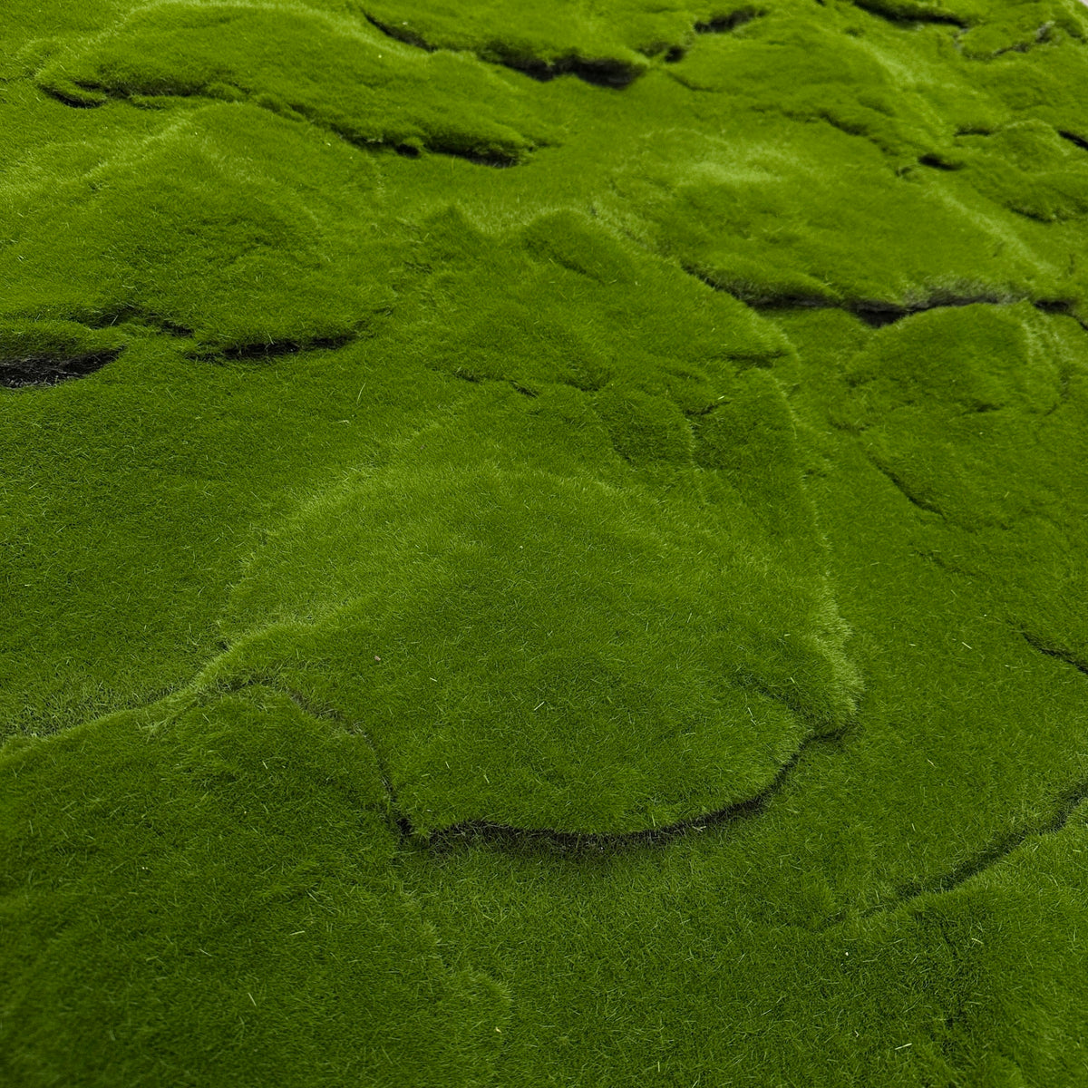 Artificial moss panel close-up, dense green lumpy texture with shallow ridges