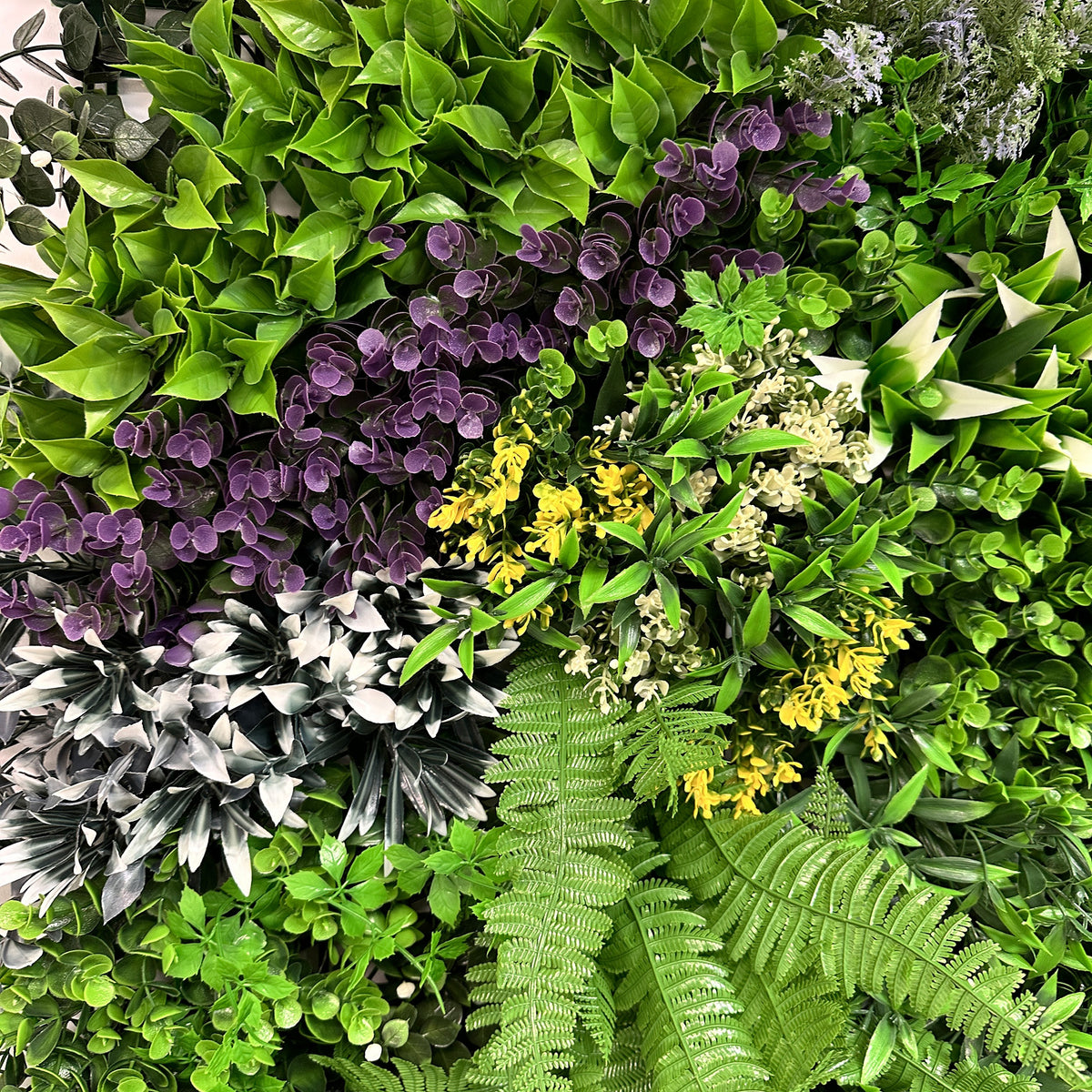 Artificial green wall panel closeup with green foliage and purple, yellow, and white flower accents