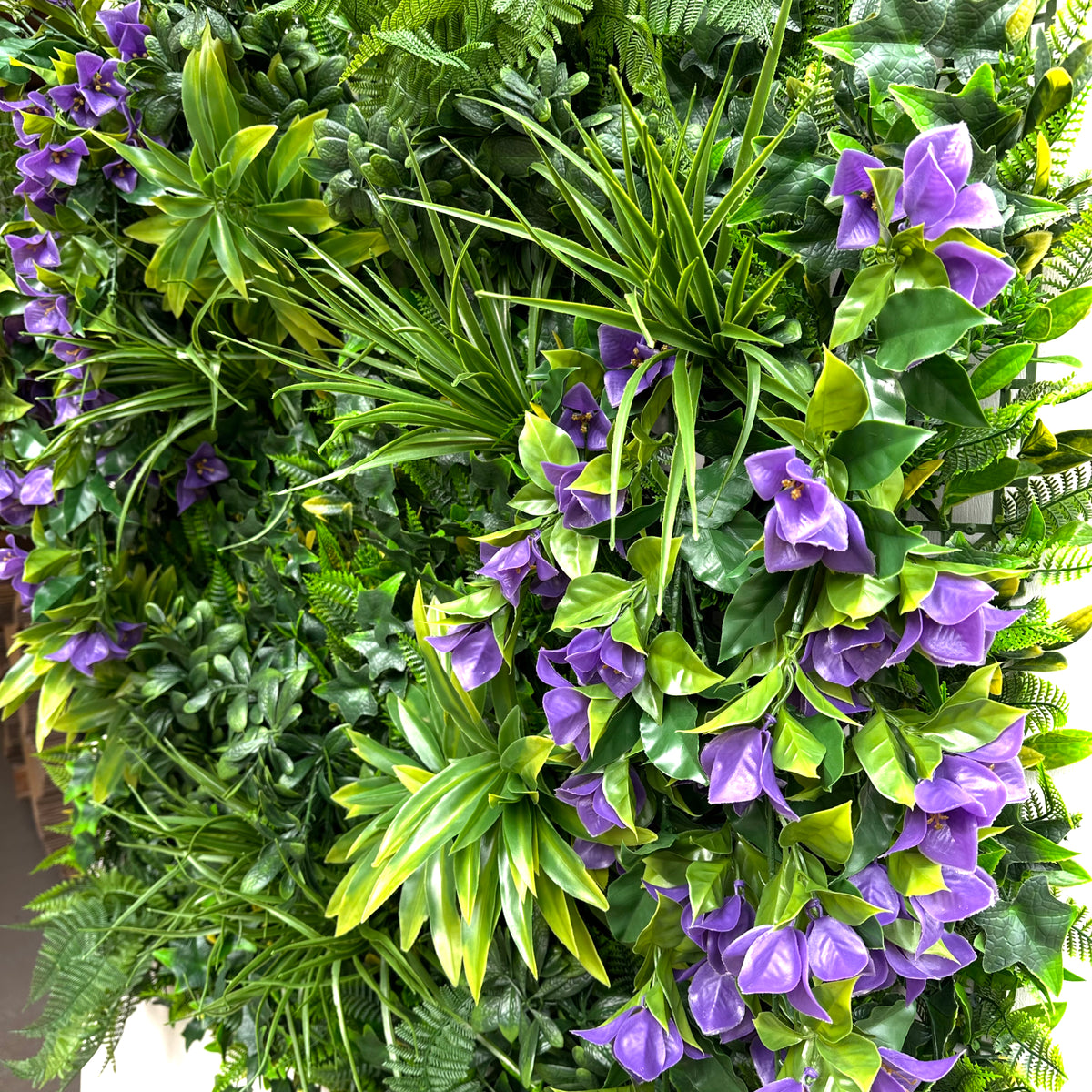 Artificial foliage wall panel closeup with purple bougainvillea-style flowers and green leaves