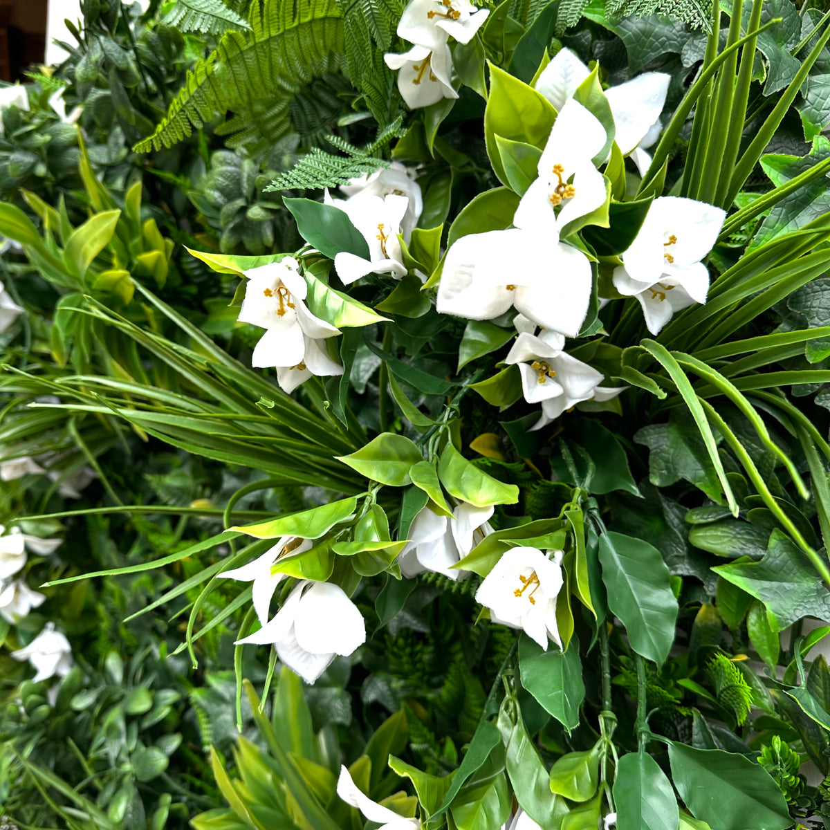 Artificial foliage wall panel with white bougainvillea-style blooms and layered green plants