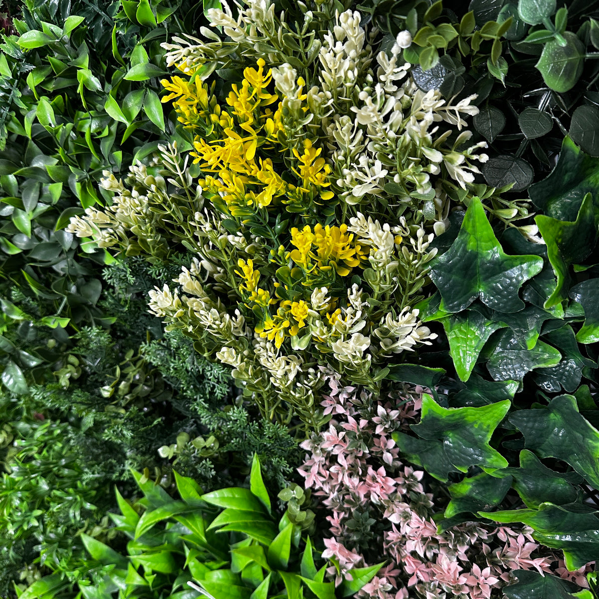 Close-up of artificial foliage wall panel with white and yellow flower clusters and dark green leaves