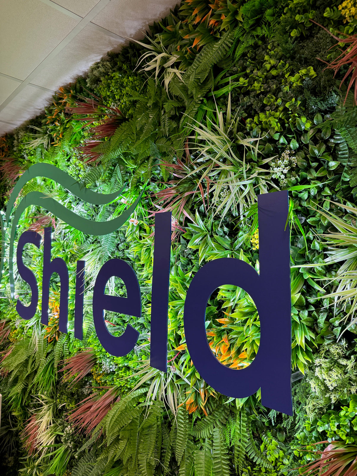 Artificial green wall panel with dense greenery and large decorative “shed” text