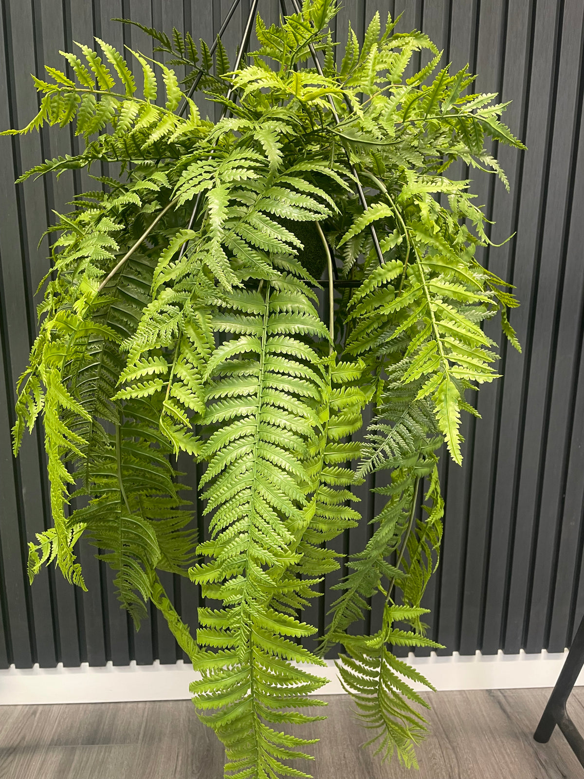 Artificial trailing fern kokedama with dark metal hanging frame and bright green fronds