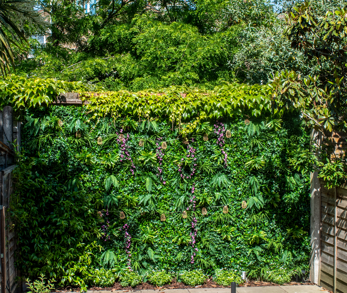 Artificial green wall panel with variegated foliage ivy palms grasses and ferns with purple trailing sweet peas 