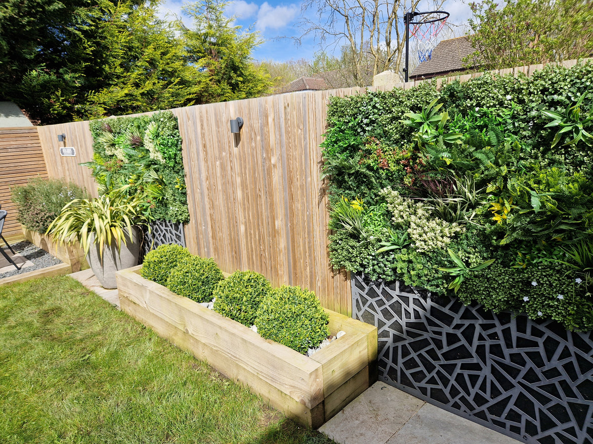 Artificial green foliage wall panel used on a raised outdoor planter with variegated leaves