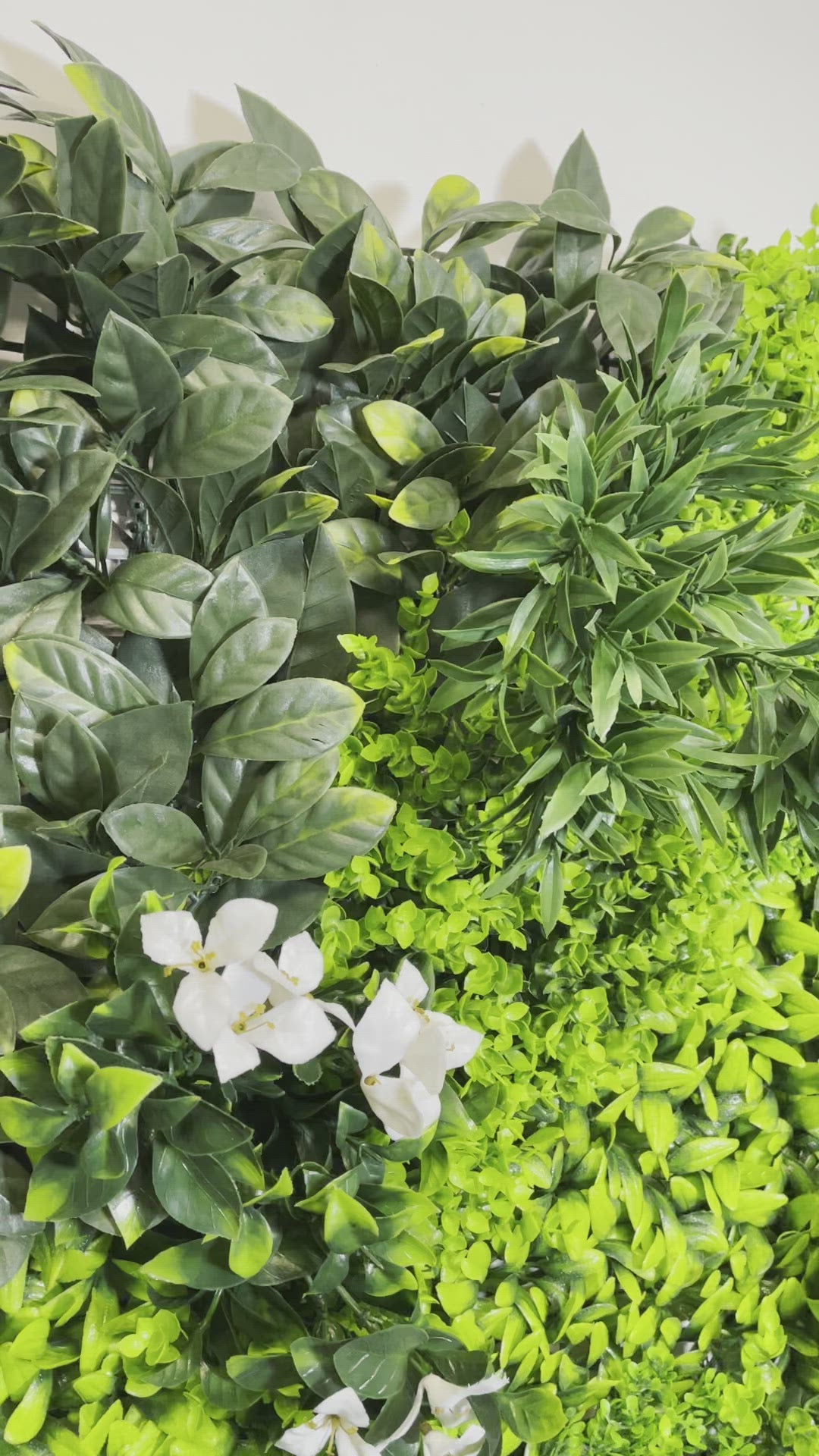 Artificial green wall panel with variegated green foliage  palms grasses eucalyptus and white flowers 100x100 cm