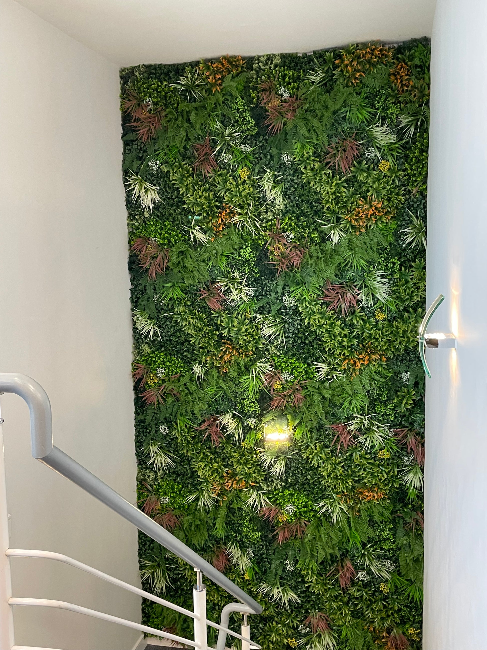 Artificial foliage wall panel with dense green leaves and scattered orange-red accents