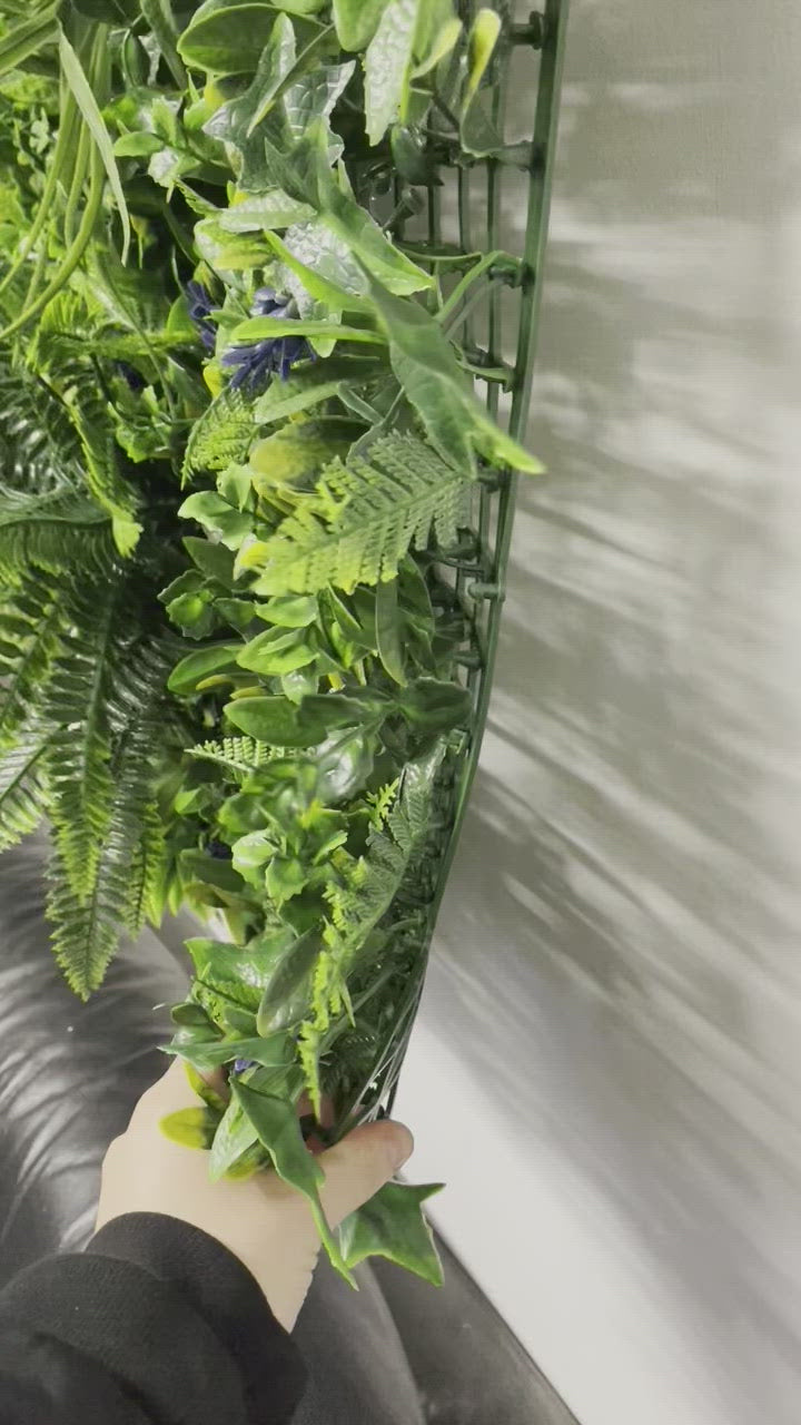 Artificial green wall panel with variegated greens of ivy, ferns, palm heads, grasses & blue-purple flowers  100x100 cm