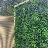 Artificial green wall panel with variegated greens of ivy, ferns, palm heads, grasses & small purple flowers  100x100 cm