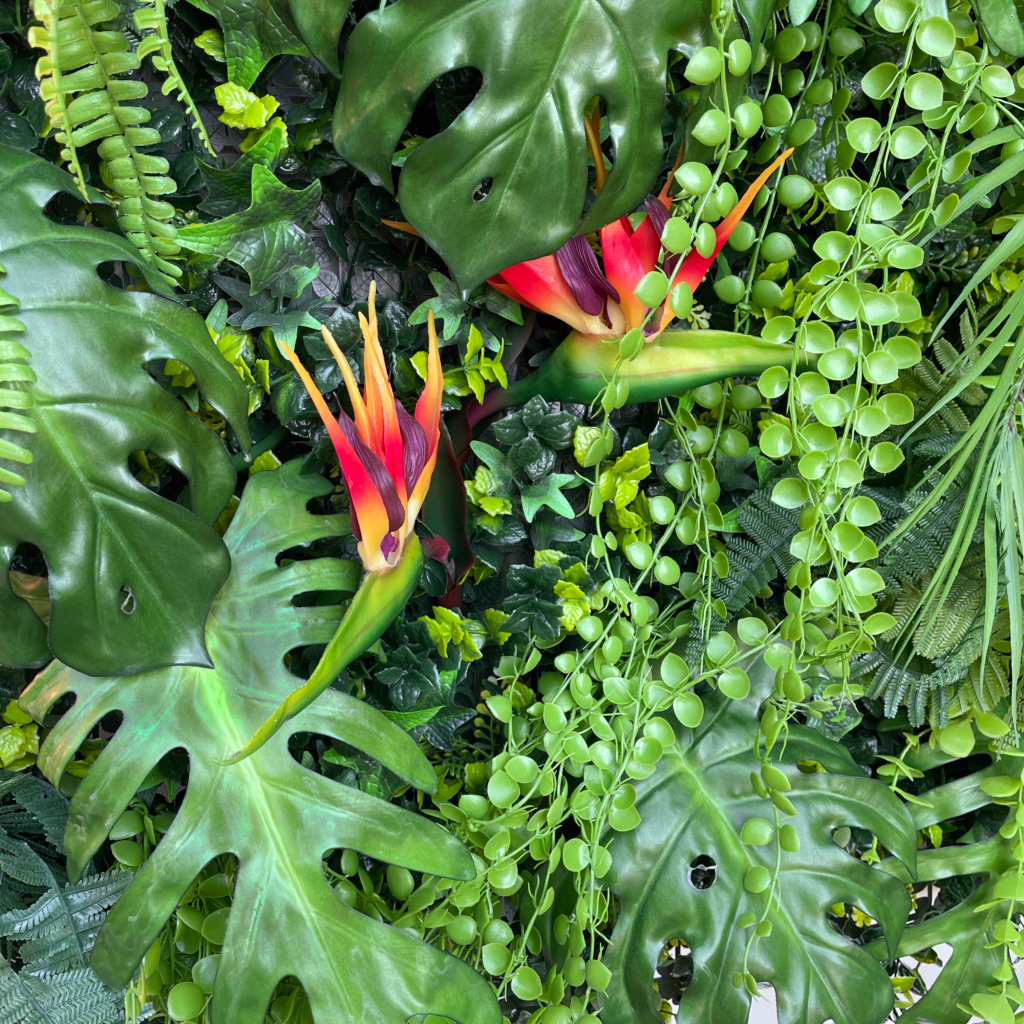 Artificial tropical plant wall foliage with glossy leaves, green bead-like vines, and red-orange blooms