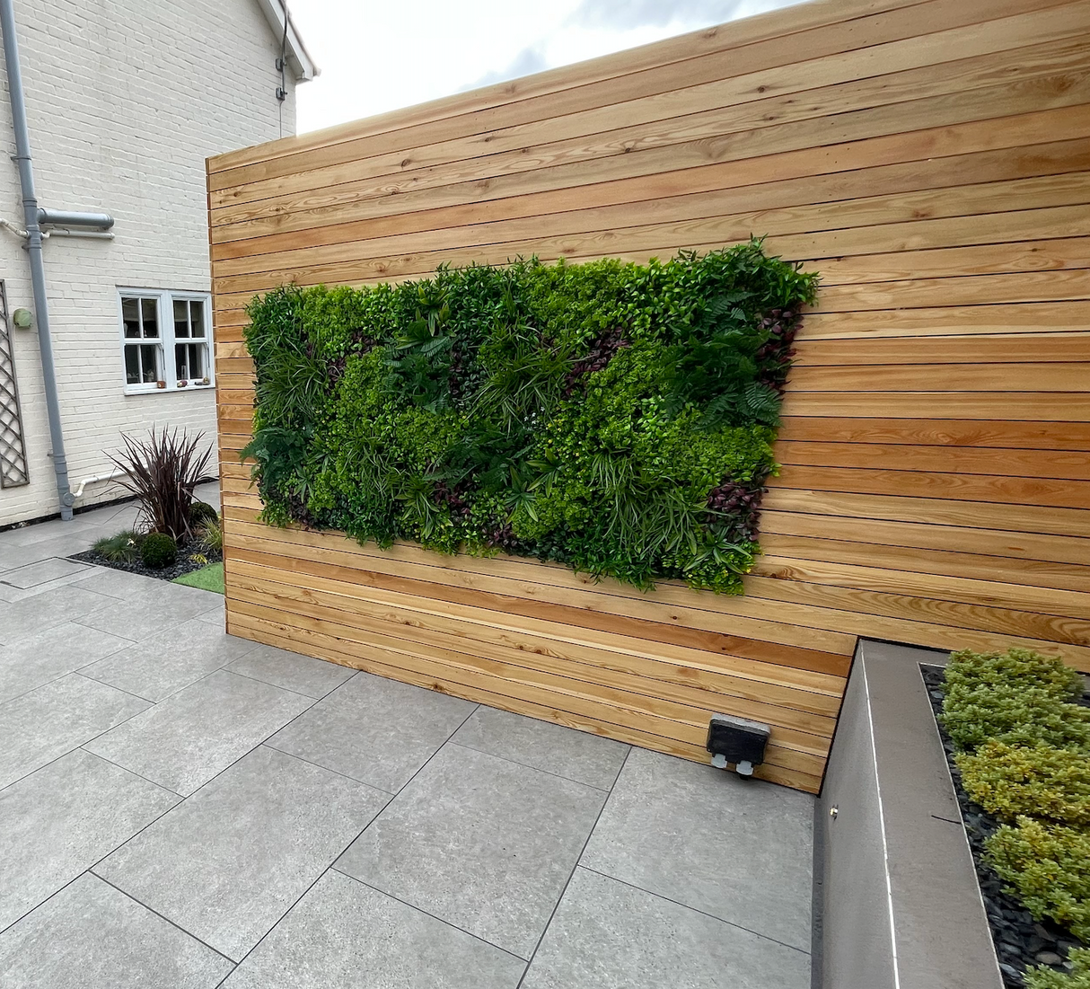 Artificial green wall panel with variegated mixed greens, palms, grasses, reds, white and yellow flowers  100x100 cm