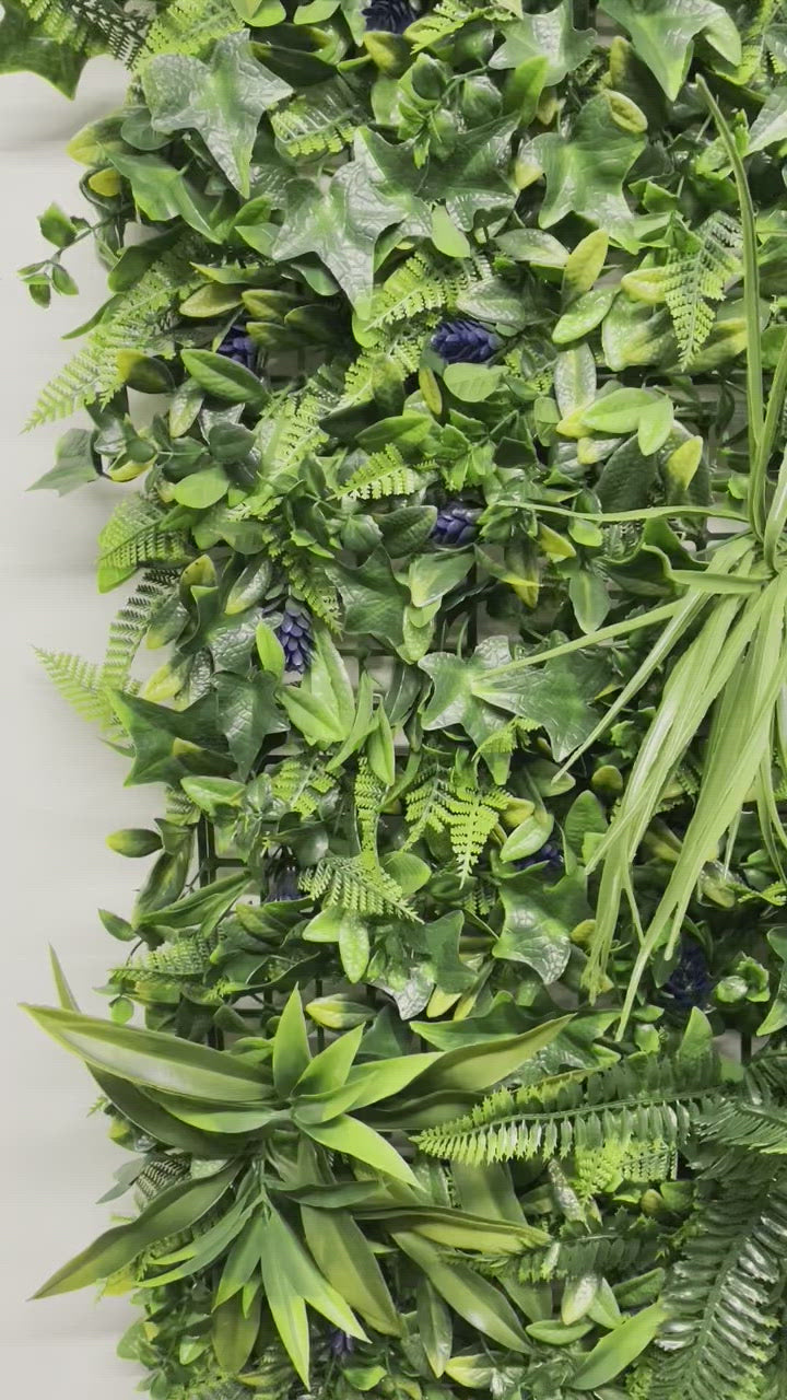 Artificial green wall panel with variegated greens of ivy, ferns, palm heads, grasses & blue-purple flowers  100x100 cm